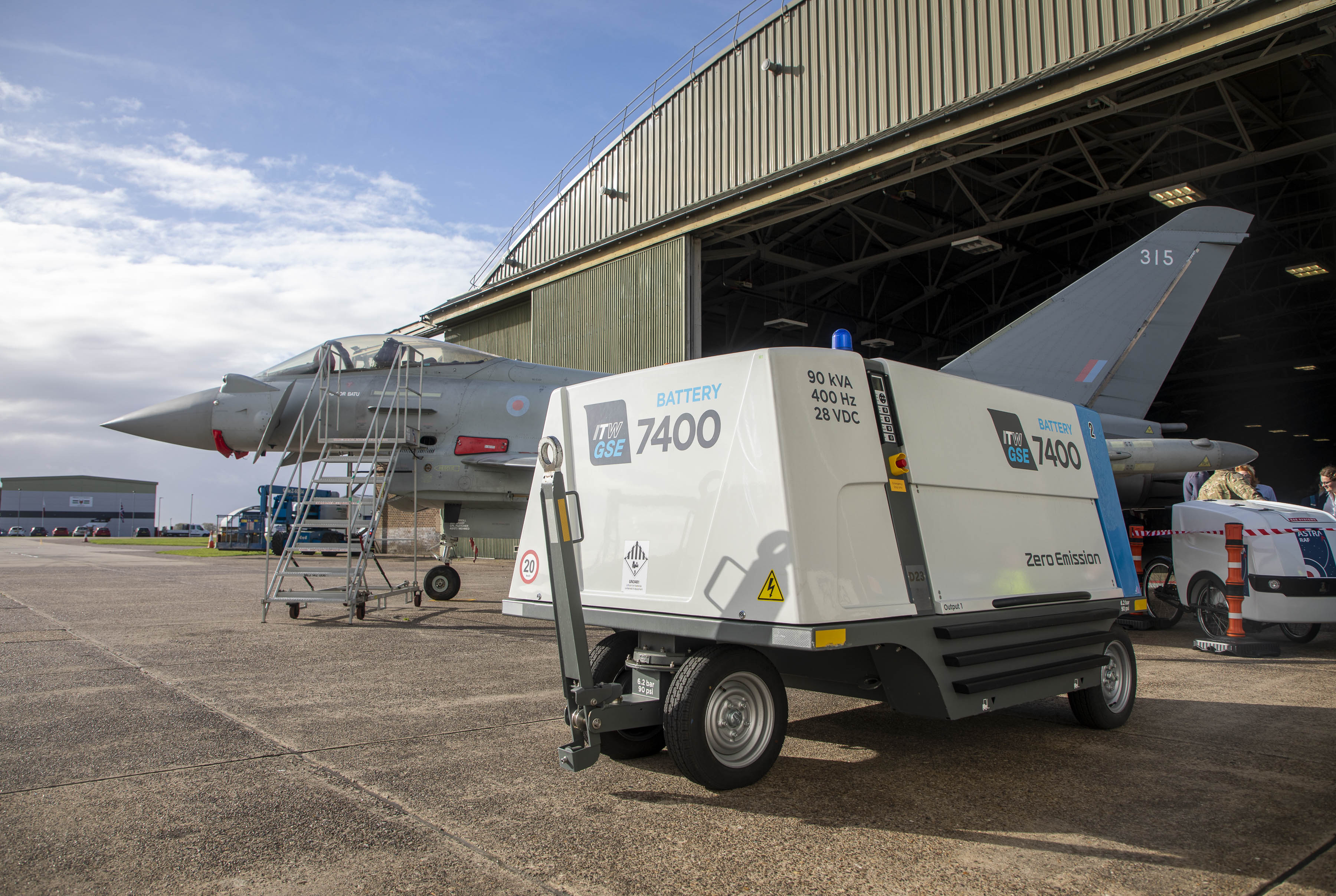 Image shows typhoon outside a hangar, with a large battery on wheels.